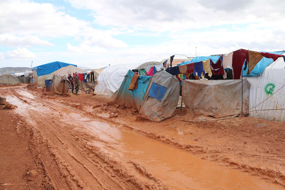 A muddy road lined with make-shift tent shelters A muddy road lined with make-shift tent shelters