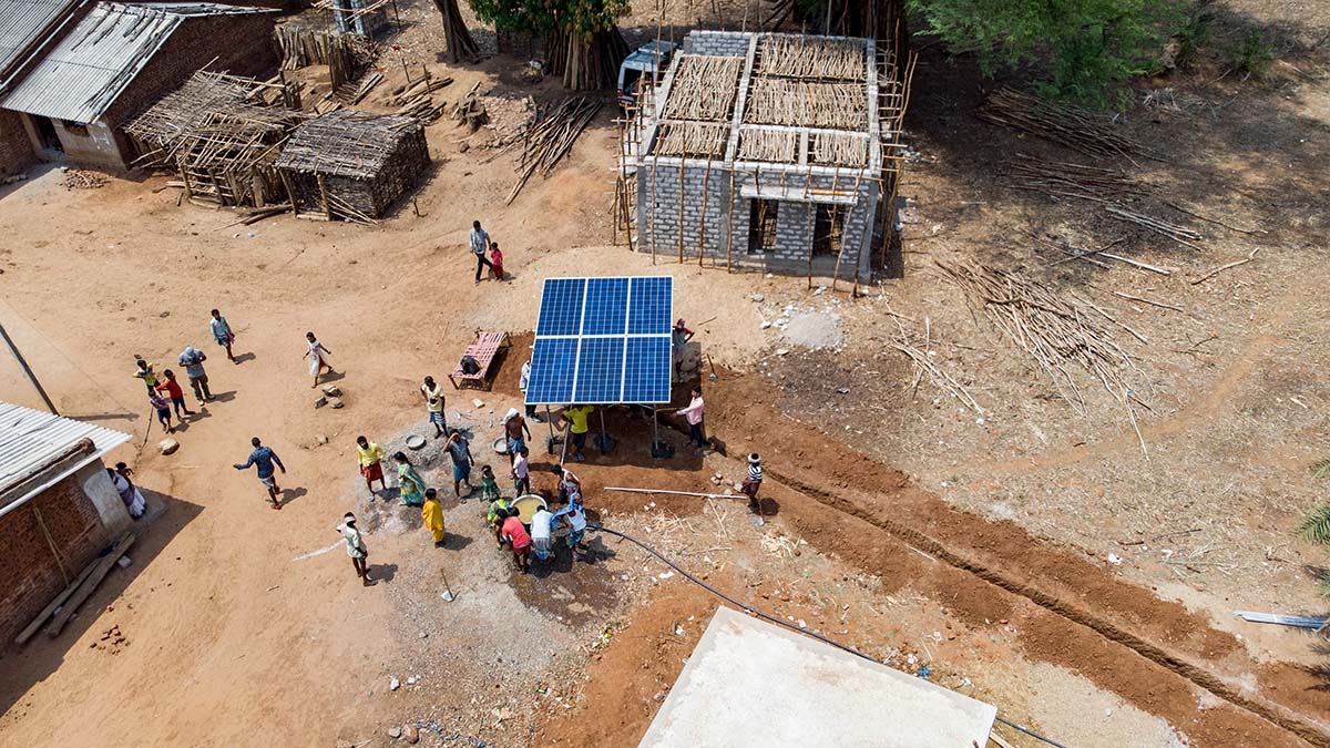 An aerial view of villagers gathered around elevated solar panels An aerial view of villagers gathered around elevated solar panels