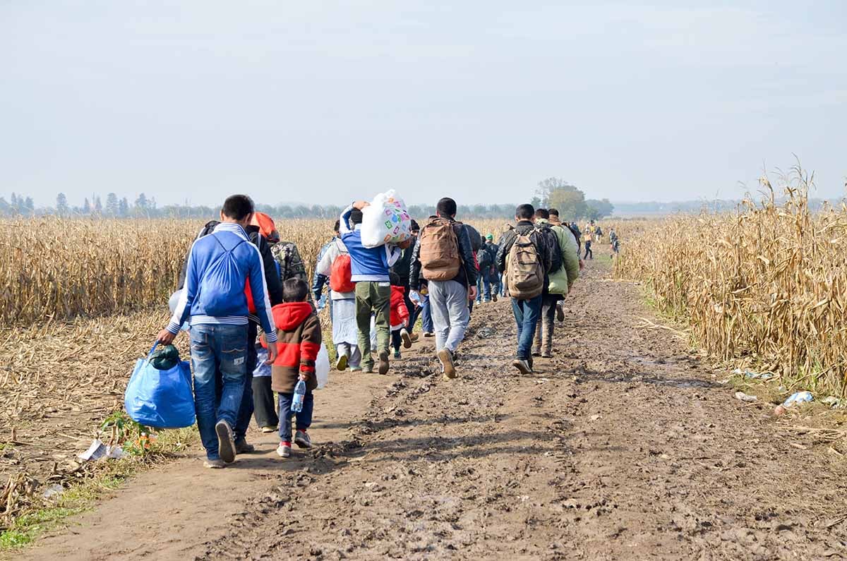 A procession of refugees walking down a dirt path A procession of refugees walking down a dirt path